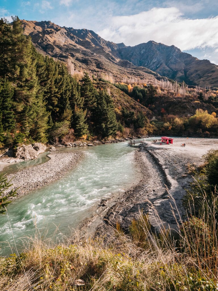 Jet boat speeding down a turquoise canyon river surrounded by alpine forest in Queenstown