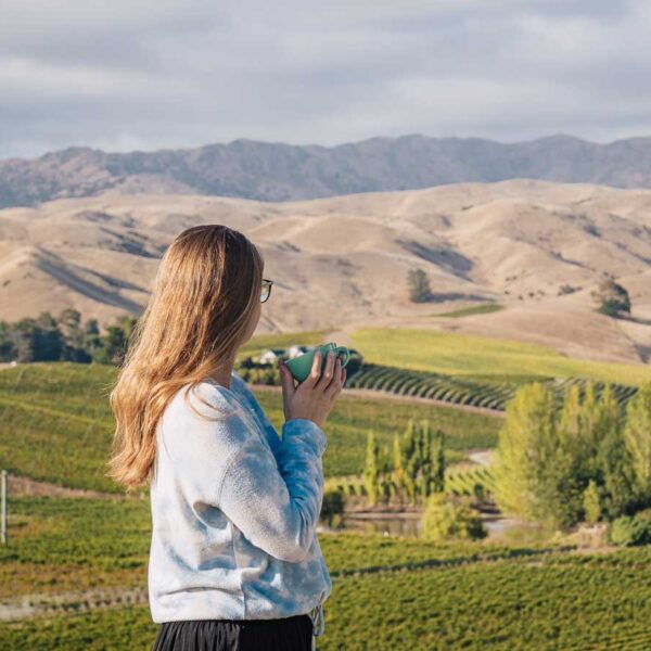 girl holding coffee cup in front of vineyard in blenheim
