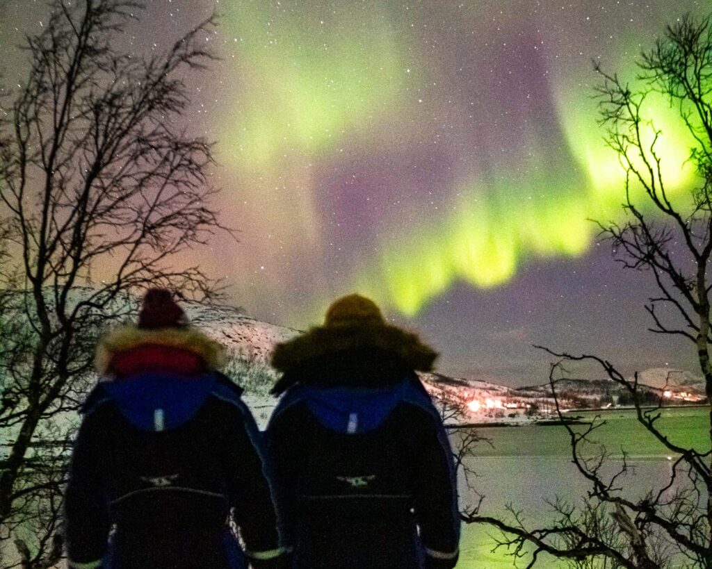 two friends travelling together standing in front of the northern lights in tromso norway