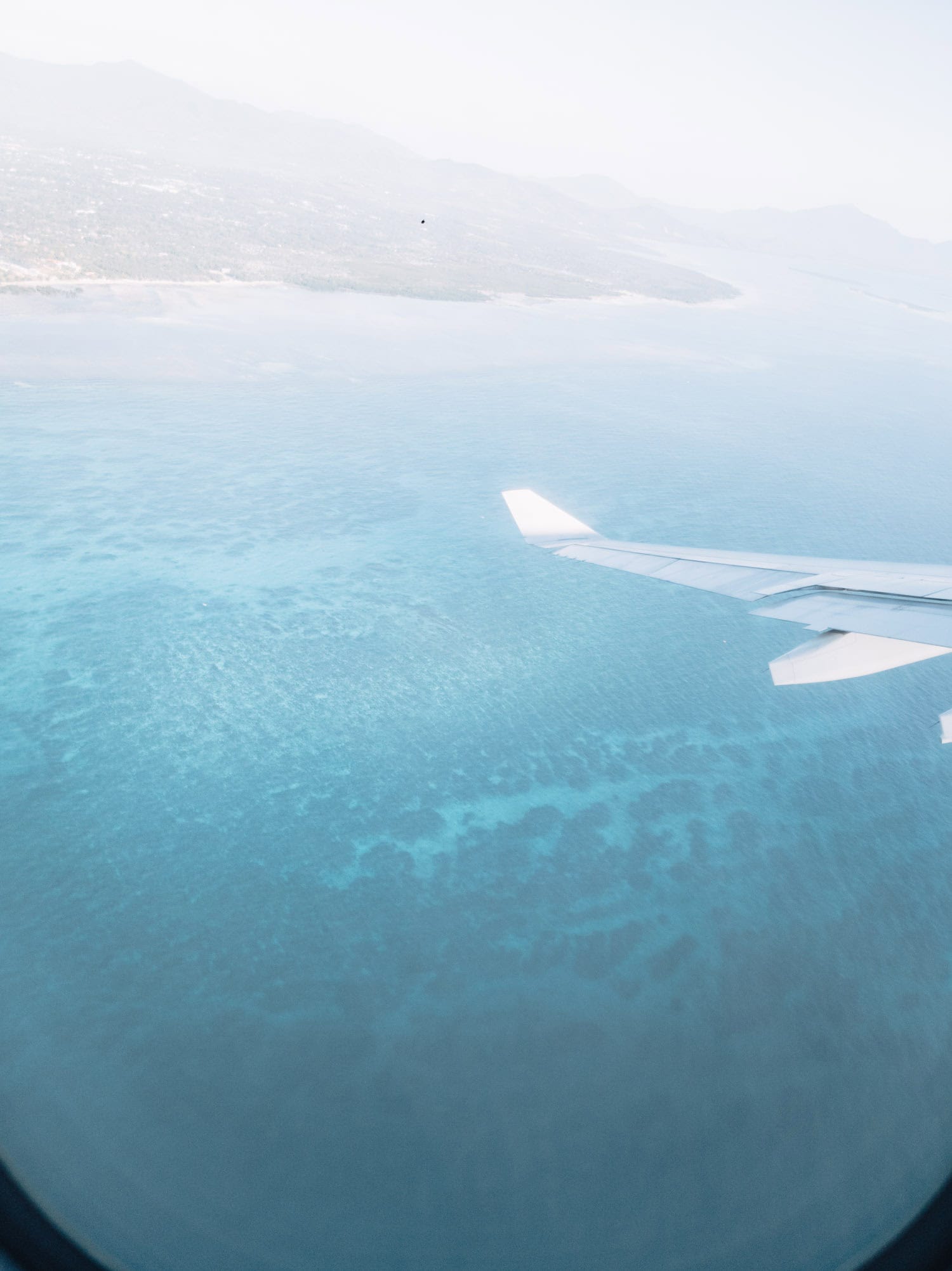 view of blue water and underwater coral reefs from the window seat of a flight in the Philippines