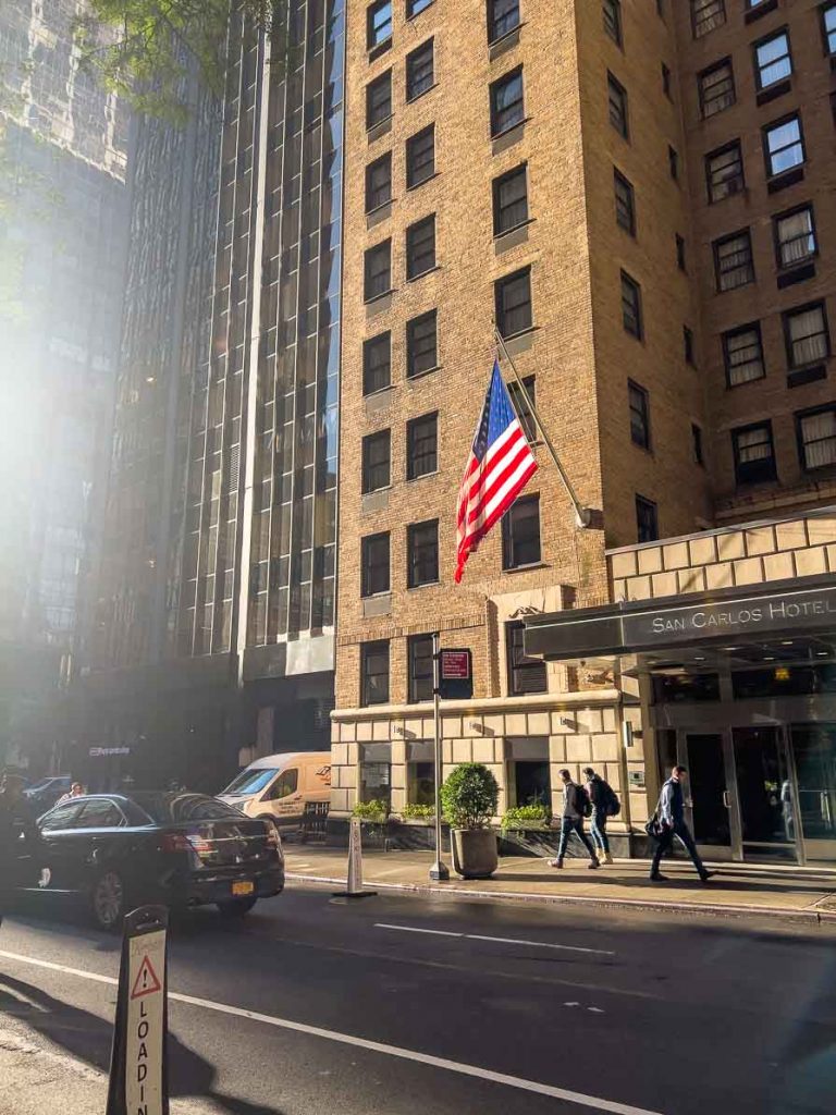 A USA flag waving outside a New York City hotel with cars driving past