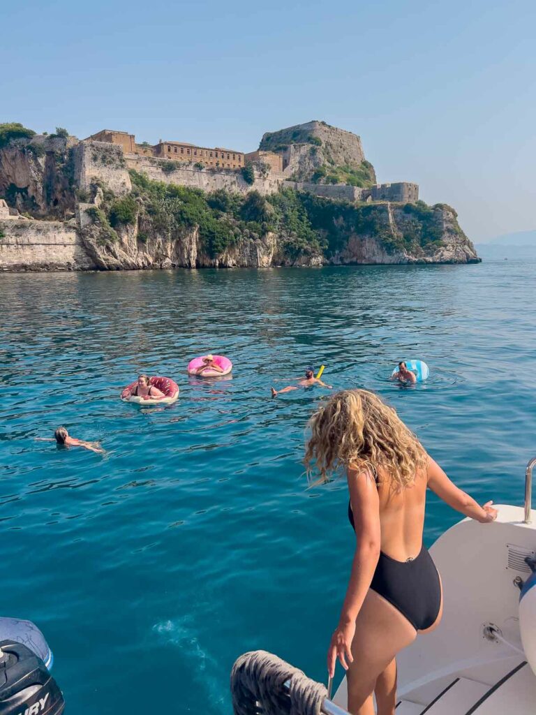 Travelers enjoying a swim in the clear waters of the Ionian Sea, with the imposing Old Fortress of Corfu providing a historic backdrop, captured during a MedSailors Greece sailing tour