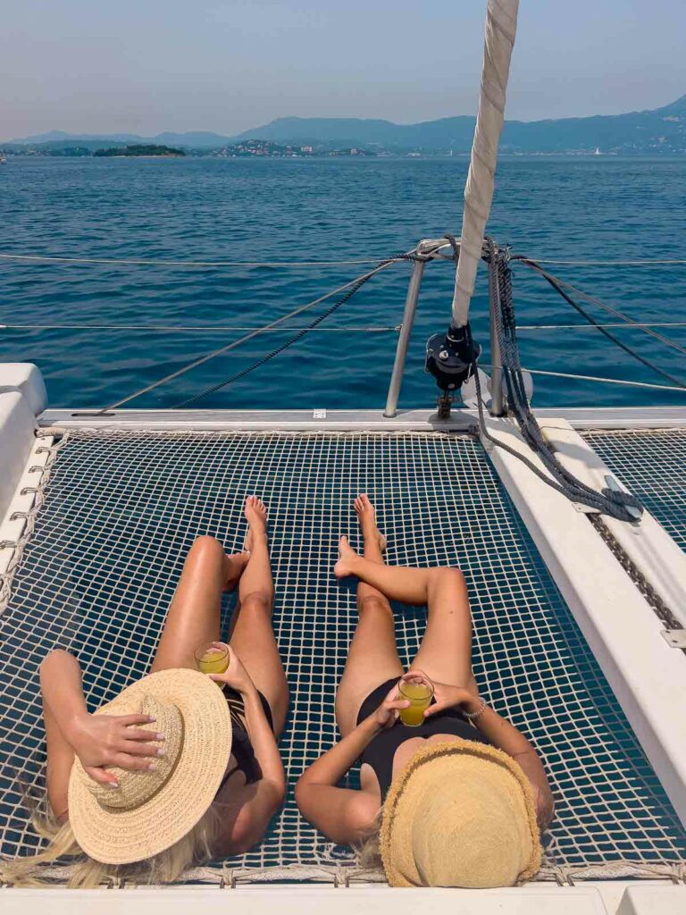 Two girls lounging on the netting of a catamaran, soaking up the sun against the serene backdrop of the deep blue Mediterranean Sea on a MedSailors Greece tour