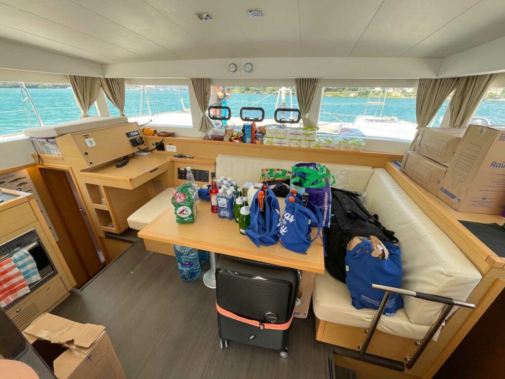 The interior dining area of a MedSailors catamaran, filled with natural light and scattered with guests' belongings, ready for communal meals and socializing
