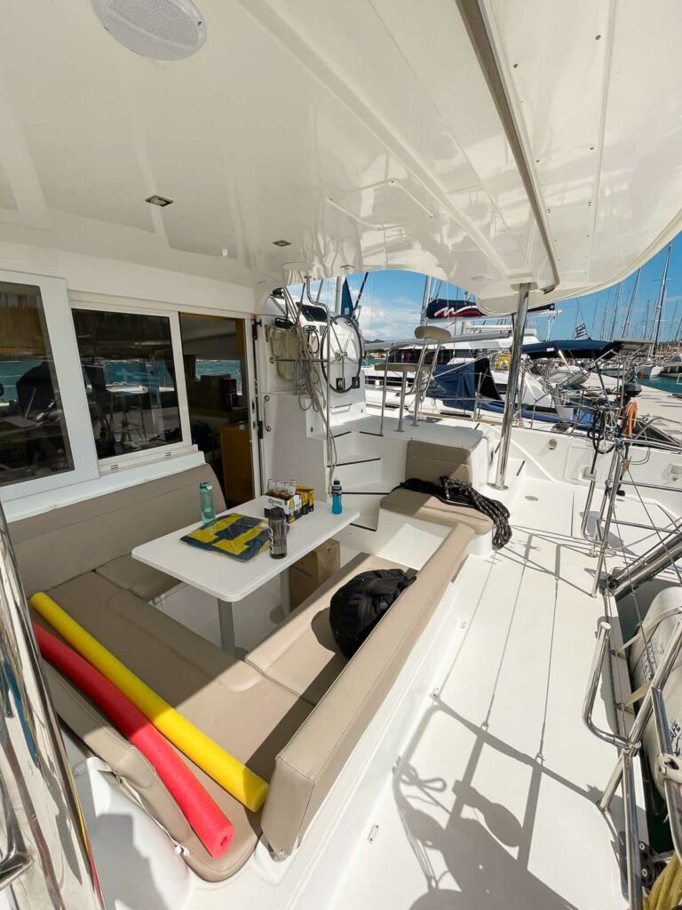 The spacious back deck of a MedSailors catamaran, equipped with a comfortable seating area and colorful floaties, ready for leisure at the marina under the bright Greek sun