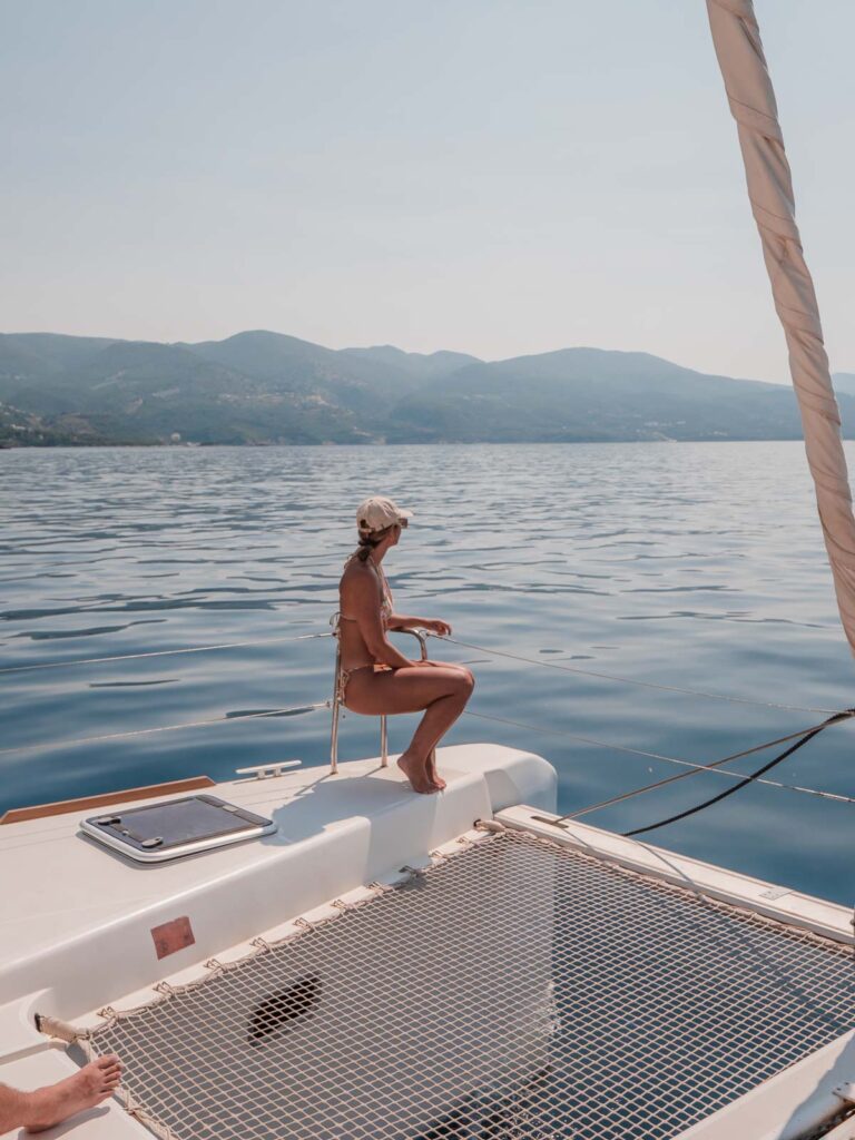 A woman sits contemplatively on the net of a catamaran, surrounded by the serene waters of Greece, on a peaceful MedSailors tour
