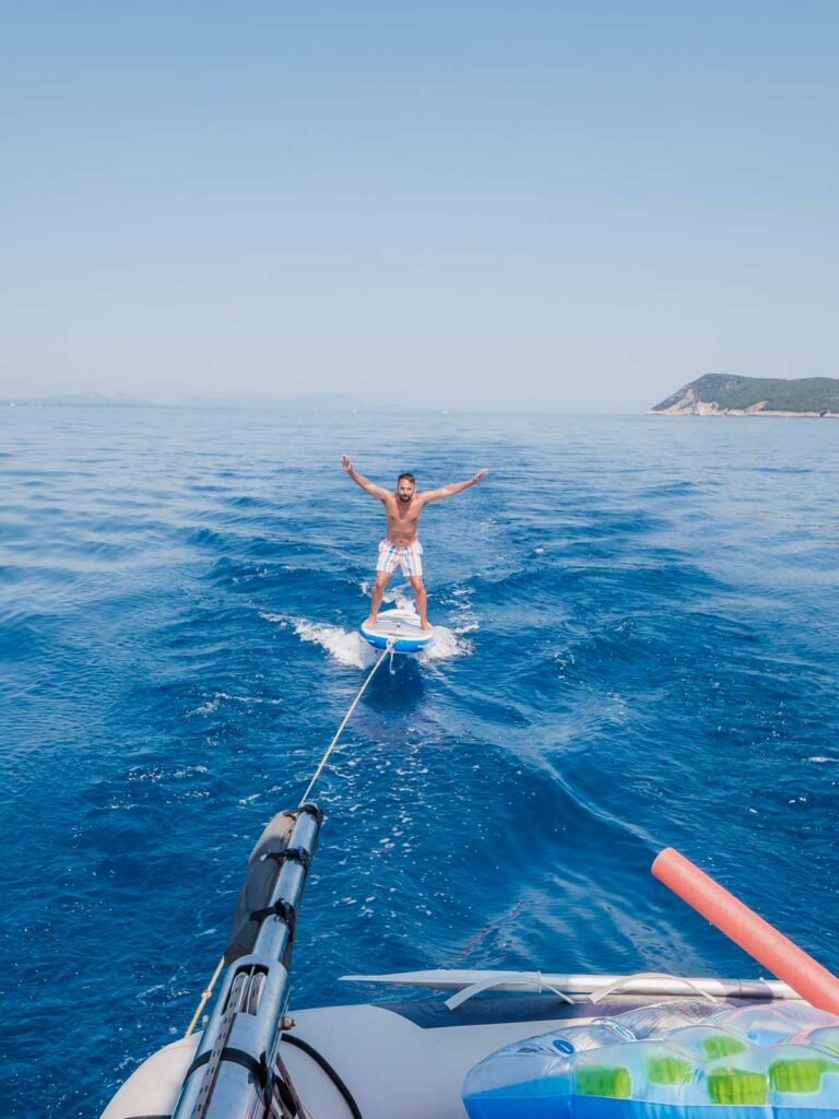An adventurer balances on a paddleboard, towed behind a boat, with arms outstretched in a pose of freedom on the glistening waters