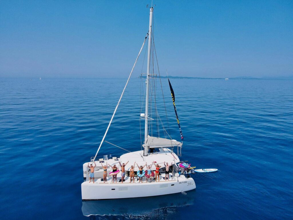 A group of travelers gathered on a MedSailors catamaran, sailing the tranquil blue waters of the Greek Ionian Sea under a clear sky