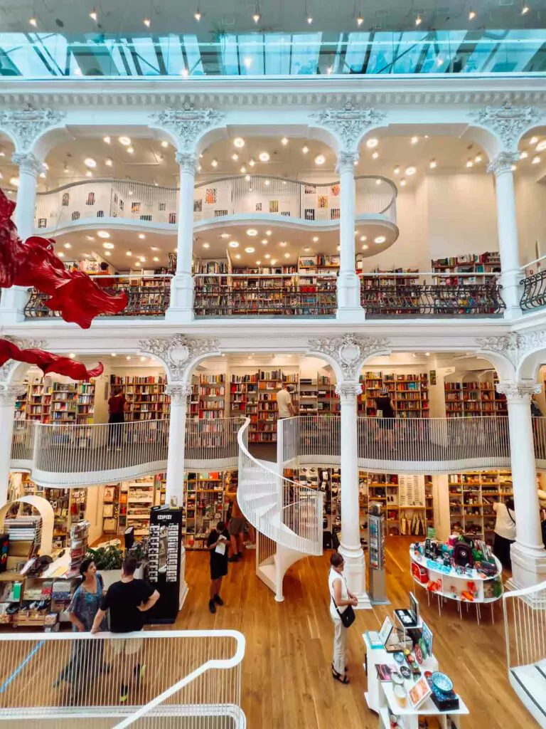 Interior of Cărturești Carusel bookstore in Bucharest, featuring multi-level white balconies filled with books, an elegant spiral staircase, and shoppers browsing in the spacious, light-filled atrium