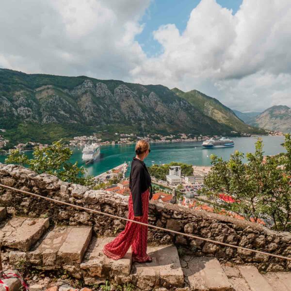 A person standing on the ancient stone walls overlooking the Bay of Kotor with the historic town and mountainous landscape of Montenegro in the background