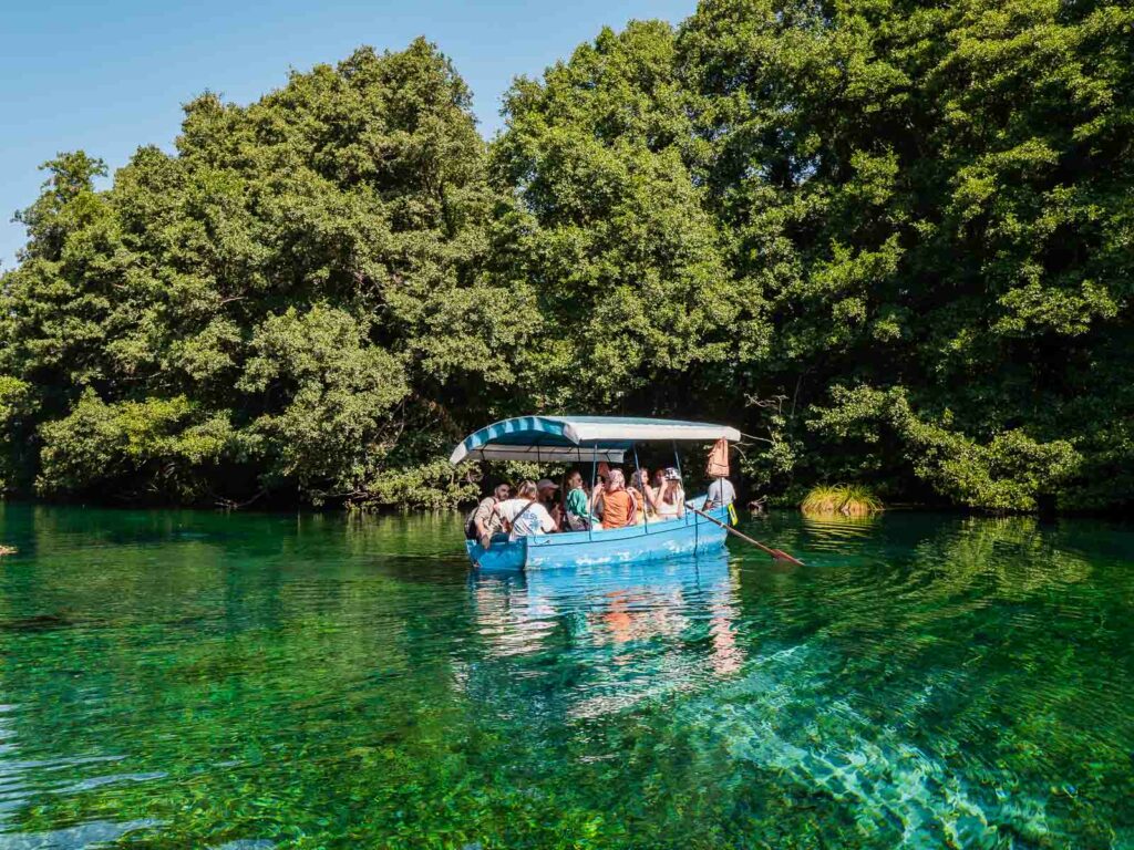 Tourists on a boat tour at the crystal-clear Ohrid Springs in North Macedonia, surrounded by lush greenery, in a serene natural setting