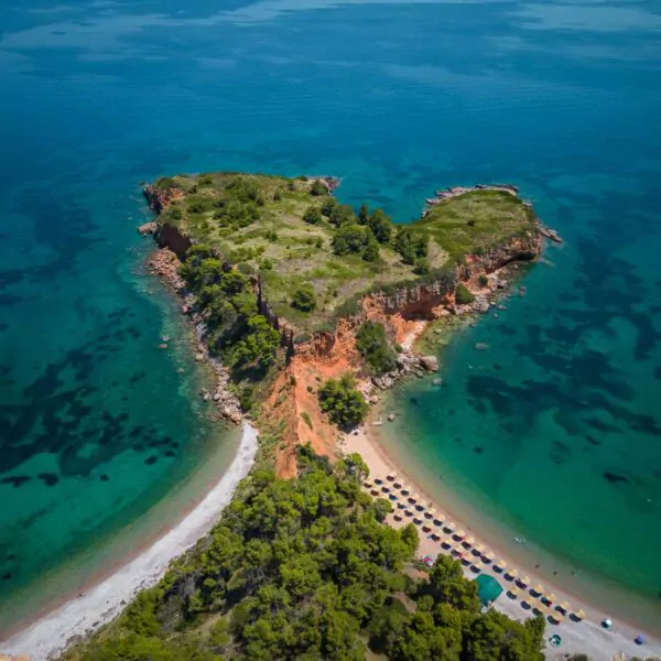 Aerial view of a Kokkinokastro Beach in Alonissos, showcasing the island's pristine travel appeal with crystal-clear turquoise waters, boats gently bobbing by the shore, and characteristic red-roofed buildings amid lush greenery