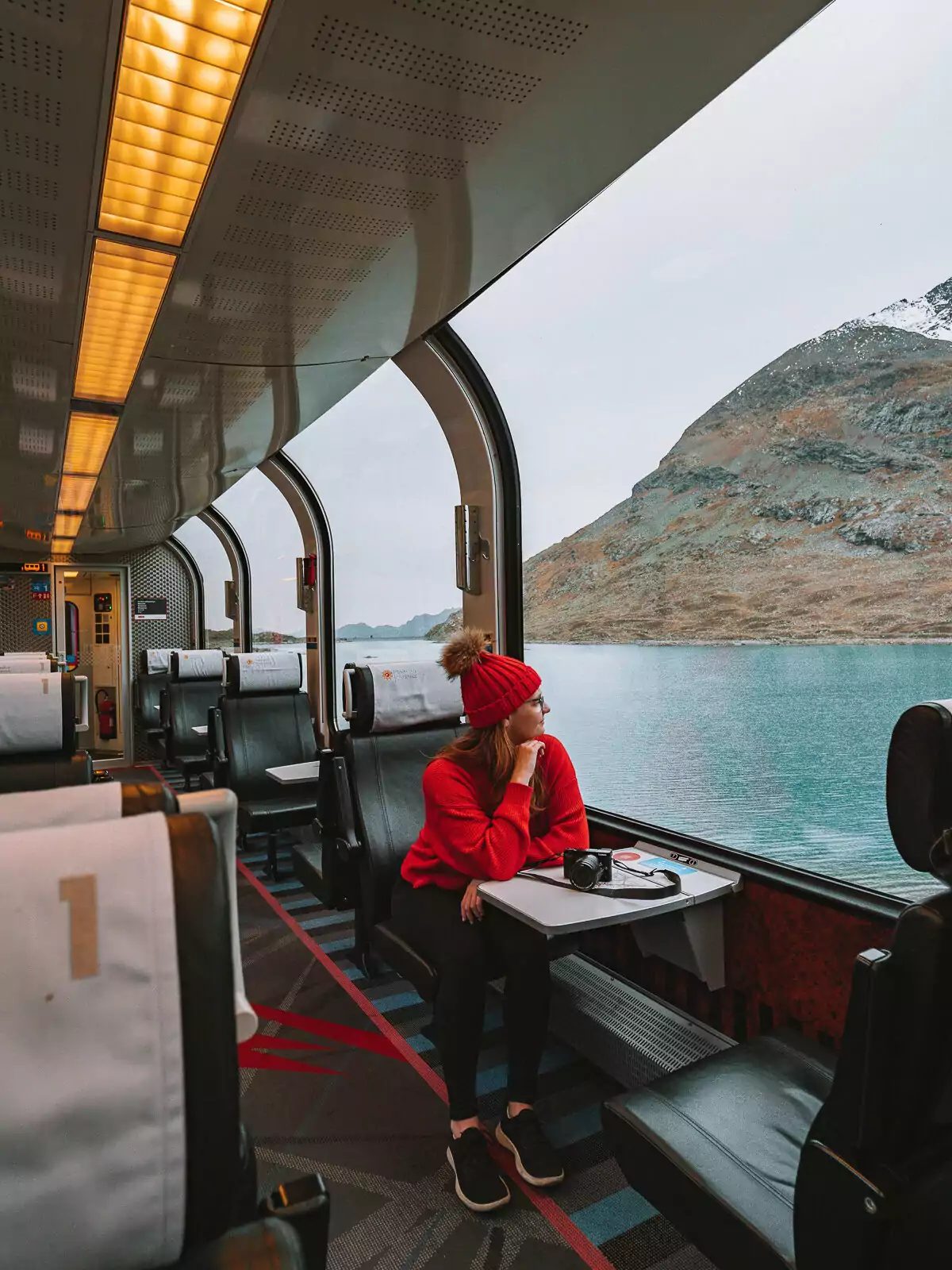 Interior view of the 1st class Bernina Express panoramic train car with passenger in red jacket enjoying scenic mountain views