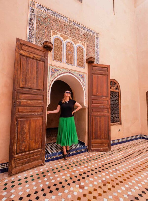 A visitor stands at the entrance of an ornately decorated doorway at Bahia Palace in Morocco, with intricate mosaic tiles and richly carved wooden doors, highlighting the architectural grandeur of the palace