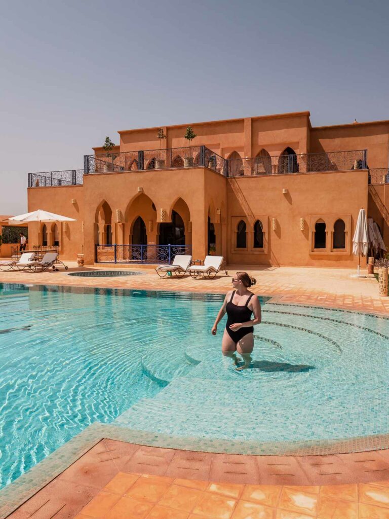 A guest relishes the cool waters of the pool at Atlas Widan, with the terracotta architecture and clear blue sky setting a serene scene, perfect for a weekend in Marrakech