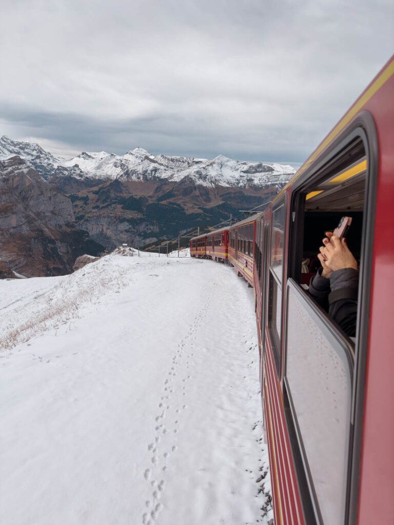 A passenger captures the moment on the iconic red train journey from Kleine Scheidegg to Jungfraujoch, with snowy alpine landscapes passing by in Switzerland