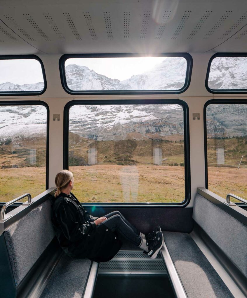 A passenger enjoys the scenic view of snow-capped mountains through large windows on a train journey from Kleine Scheidegg to Lauterbrunnen