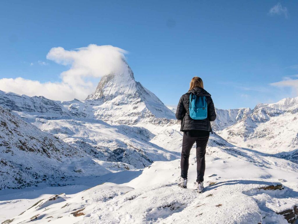 A hiker stands facing the iconic Matterhorn, its peak shrouded in clouds against a pristine snow-covered landscape, a breathtaking moment on a ten day Switzerland itinerary