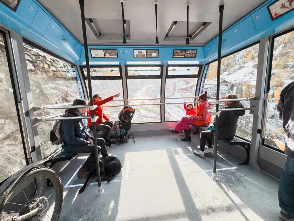 Inside the cable car ascending to Matterhorn Glacier Paradise, with passengers in ski gear anticipating the adventure ahead, framed by panoramic windows revealing the rocky terrain outside