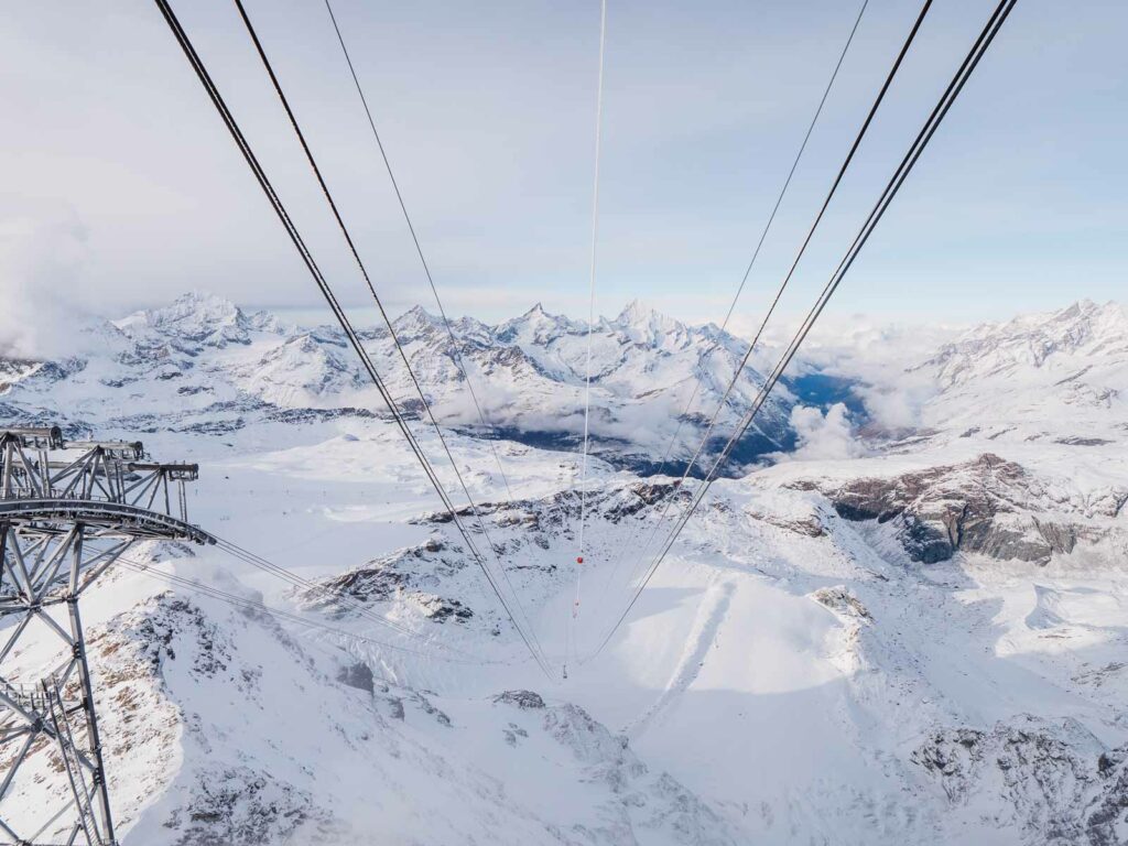 The breathtaking view from Matterhorn Glacier Paradise reveals a sea of snow-covered peaks stretching into the distance, with the stark lines of the cable car cables framing the high alpine vista