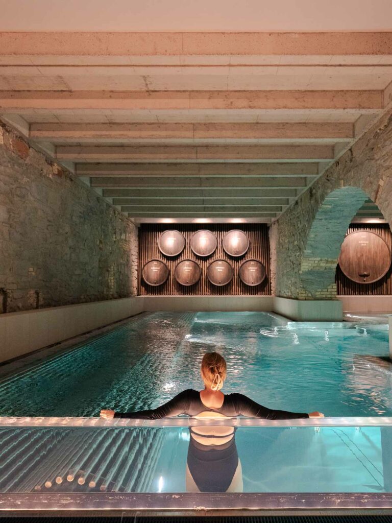A visitor unwinds in the ambient, barrel-accented thermal pools of Hürlimann Spa in Zürich, a serene and luxurious escape in Switzerland