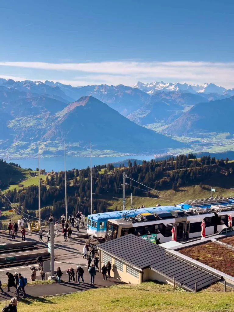The bustling summit area of Rigi Kulm, swathed in sunlight with panoramic views of the Swiss Alps and the shimmering lake below, a popular destination on a 10 day Switzerland itinerary