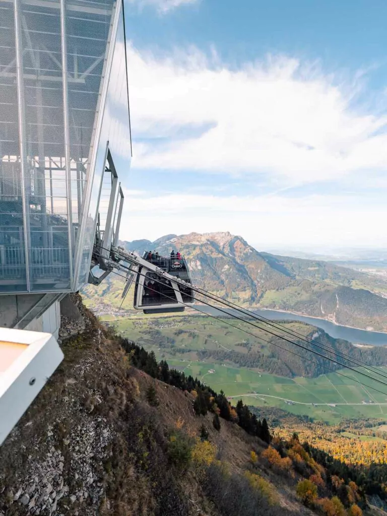 The CabriO cable car glides towards Stanserhorn's summit, offering riders an aerial view of the verdant landscape and serpentine lake below