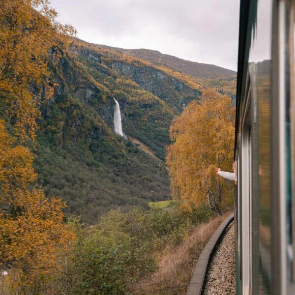A captivating view from the Flam railway, featuring autumn-coloured foliage and a distant waterfall, inviting travellers to ponder 