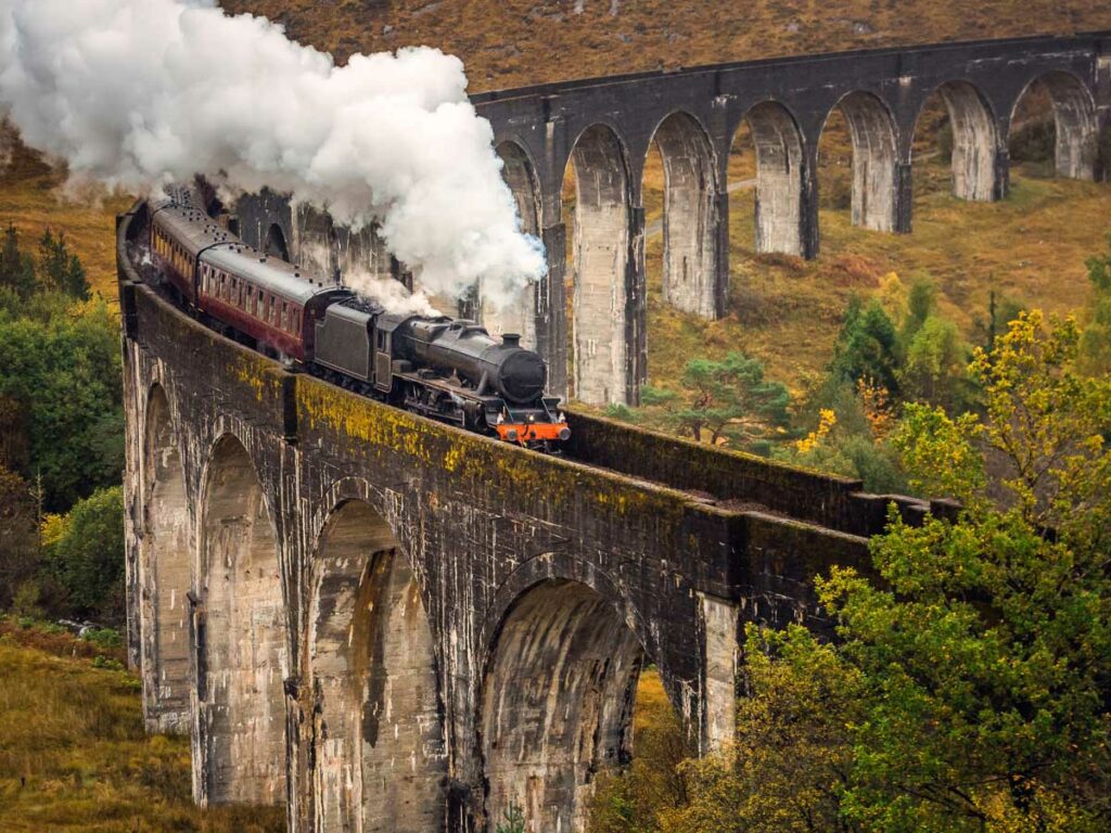 A vintage Jacobite steam train chugging over the Glenfinnan Viaduct along the rugged West Highland Line, capturing one of the most beautiful train journeys in Europe