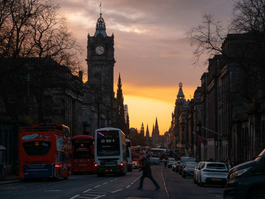 Sunset over Edinburgh with the silhouette of the city's historic architecture against a vibrant orange sky, capturing the peaceful end of a day spent travelling solo in Edinburgh
