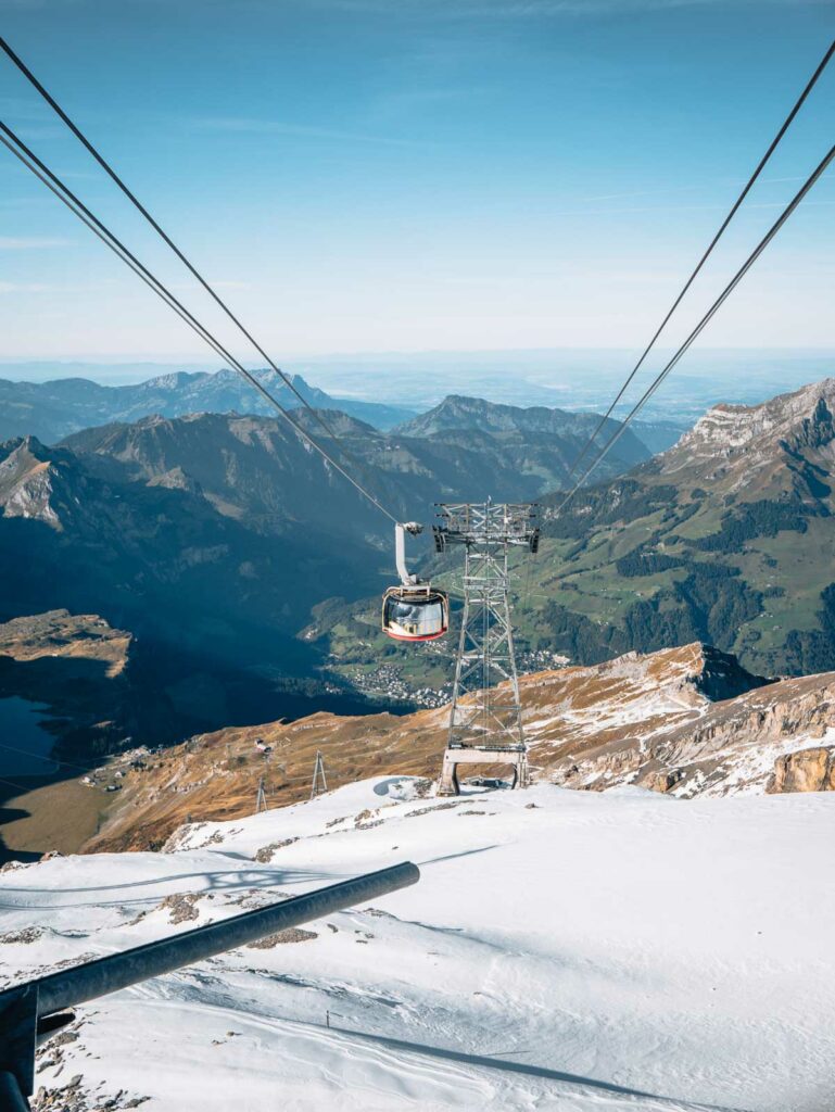 A rotating cable car glides over the crisp, snow-covered slopes of Mount Titlis, offering an expansive view of the alpine scenery, a highlight for adventure-seekers on a 'ten days in Switzerland' tour