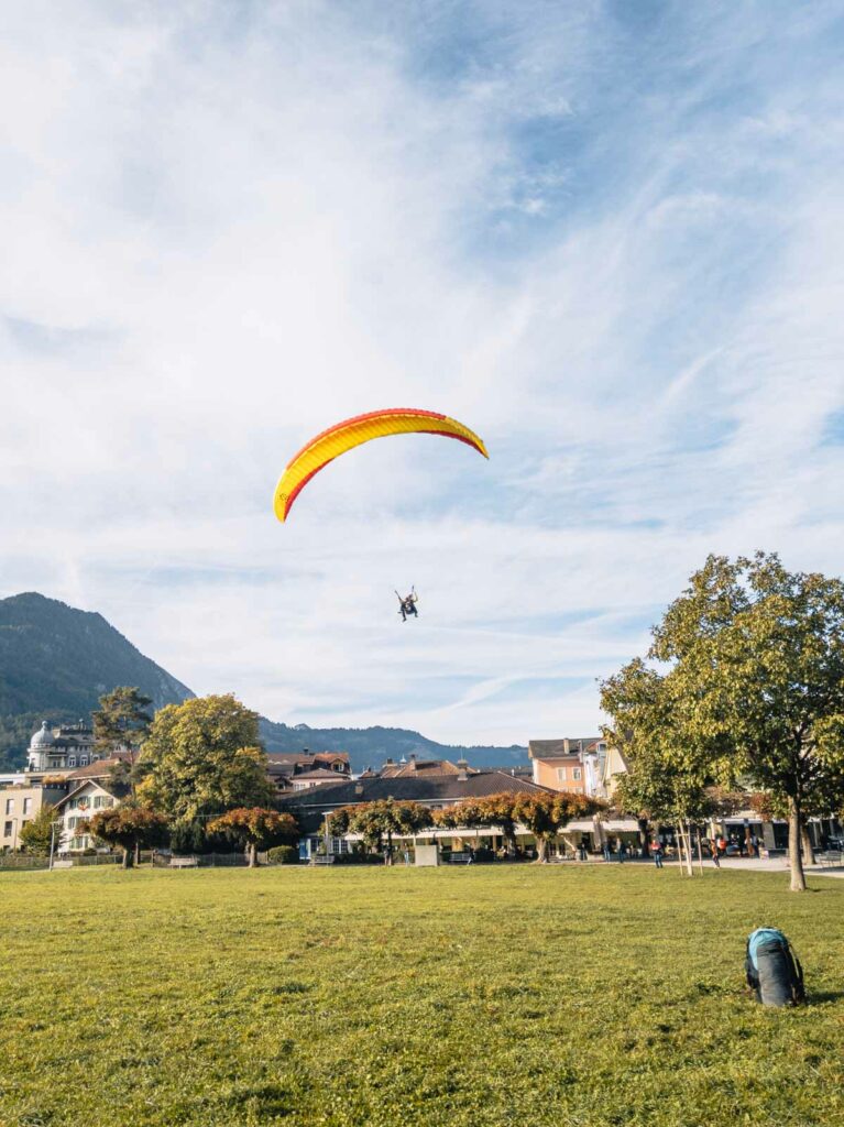 A paraglider descending onto the lush green park in Interlaken, Switzerland, as part of a thrilling ten-day Switzerland itinerary adventure