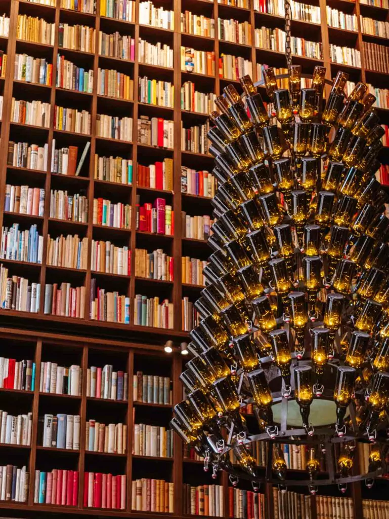 The B2 Hotel library, featuring extensive bookshelves and a unique chandelier made of beer bottles, referencing the building's history as a brewery