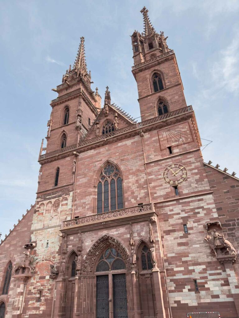 The imposing red sandstone façade and twin Gothic spires of Basel Cathedral rise majestically against a clear sky, an architectural marvel and a top thing to do in Basel