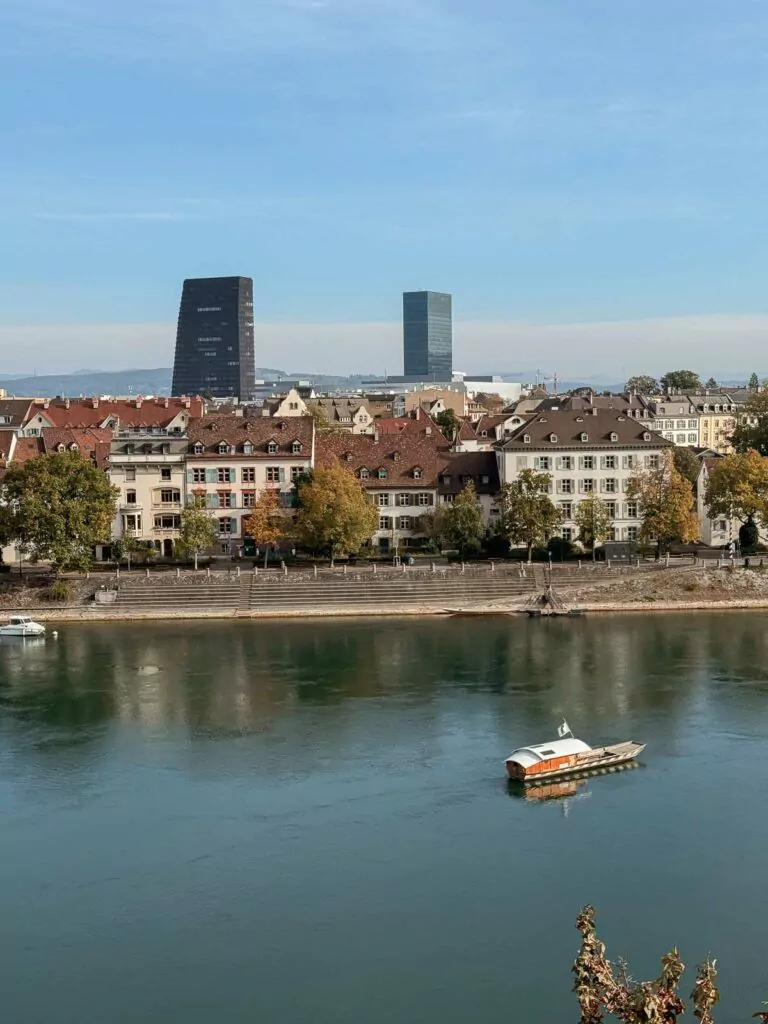 A view from Basel Cathedral overlooking the Rhine River, as a ferry crosses the tranquil waters with Basel's skyline in the background, capturing one of the many engaging activities in Basel