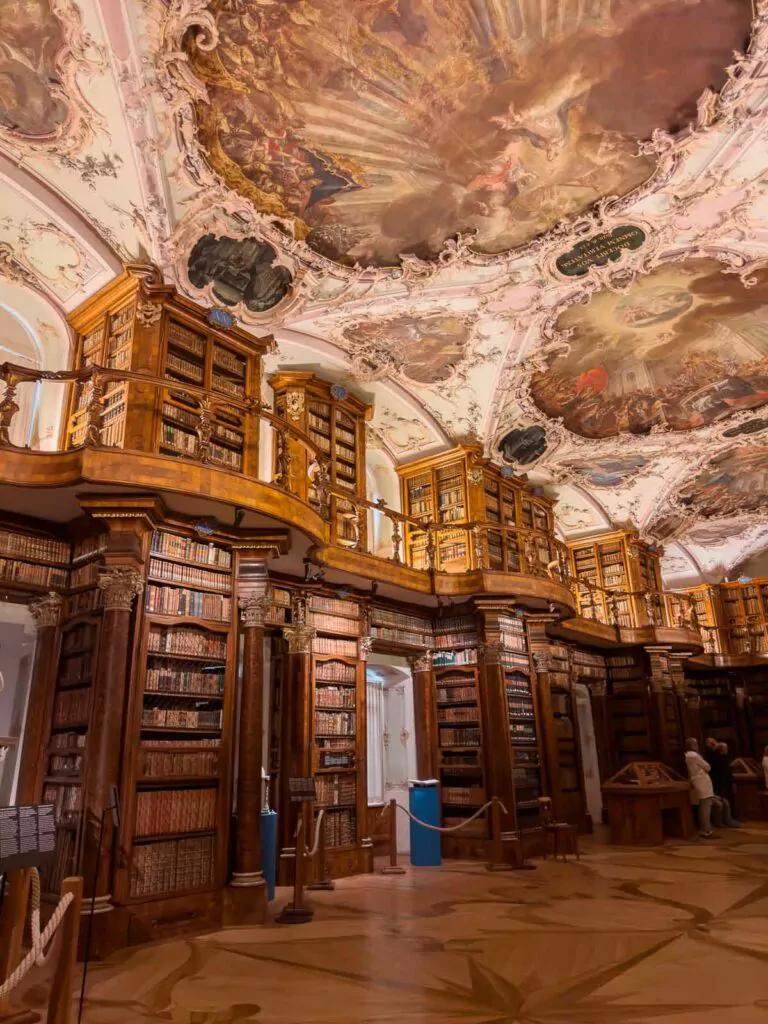 Interior view of the St. Gallen Library in Switzerland, with richly detailed wooden bookcases filled with books, a patterned floor, and an intricately frescoed ceiling