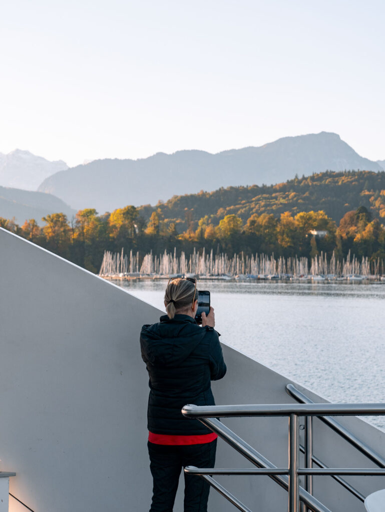A passenger captures the serene beauty of Lake Lucerne from the deck of a cruise, with the silhouette of either Mount Rigi or Pilatus in the distance