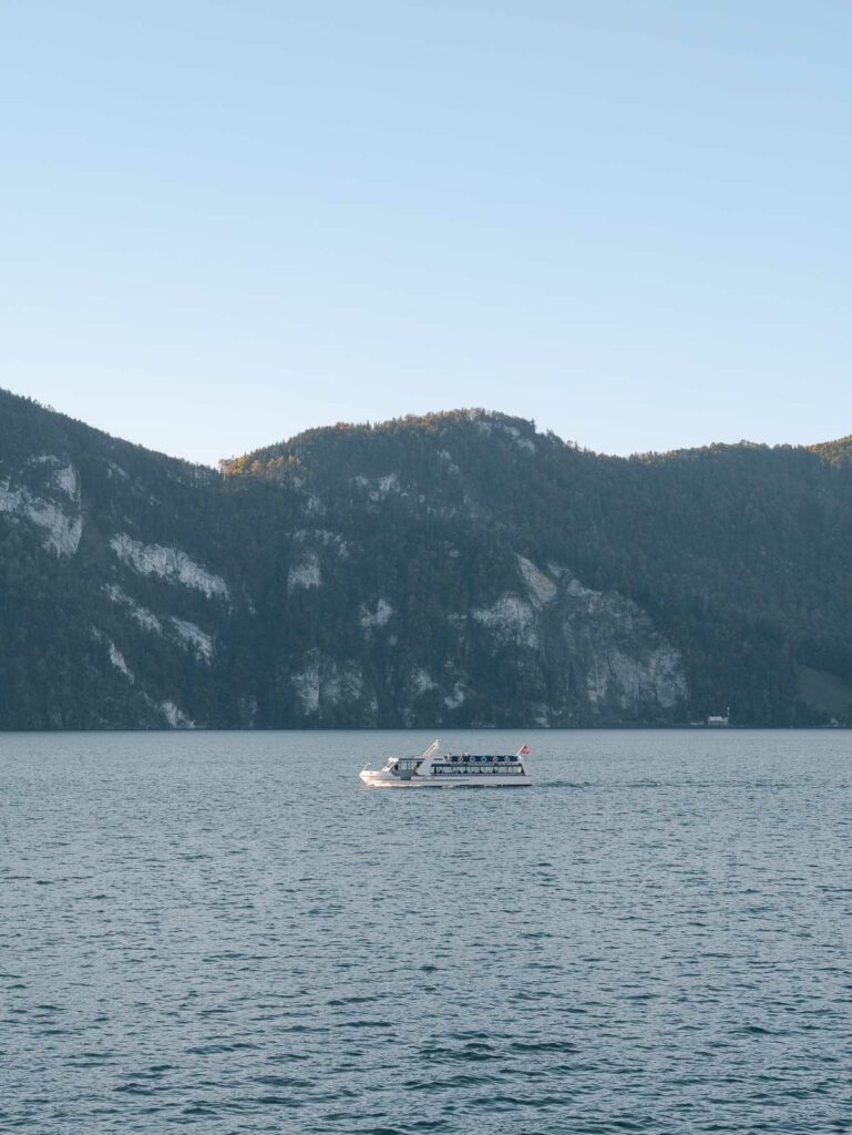 A cruise boat glides across the calm waters of Lake Lucerne, flanked by the steep, forested slopes of the surrounding Swiss mountains