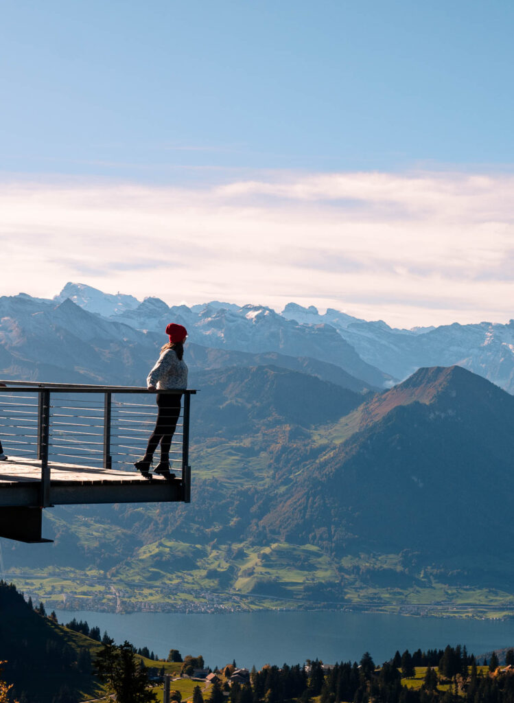 Alexx with a red hat stands on an observation deck on Mount Rigi, taking in the panoramic view of the Swiss Alps and Lake Lucerne, a highlight for those exploring with a Lucerne Travel Pass
