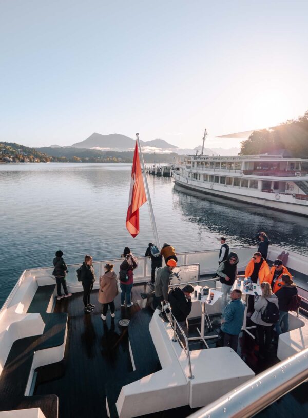 Passengers enjoy a tranquil cruise on Lake Lucerne, with the peaks of Pilatus and the Swiss Alps in the distance, a serene experience complementing the adventure of ascending mountains like Titlis or Rigi