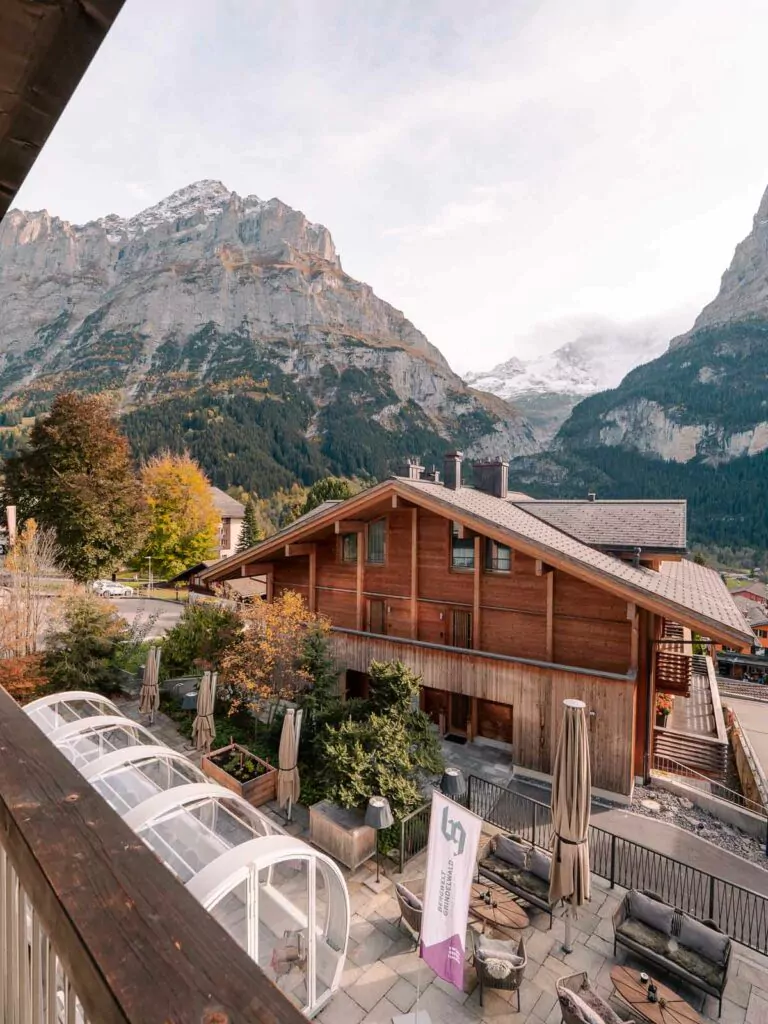 View from the Bergwelt Hotel in Grindelwald showing a traditional wooden chalet with a backdrop of alpine mountains and a terrace with seating pods