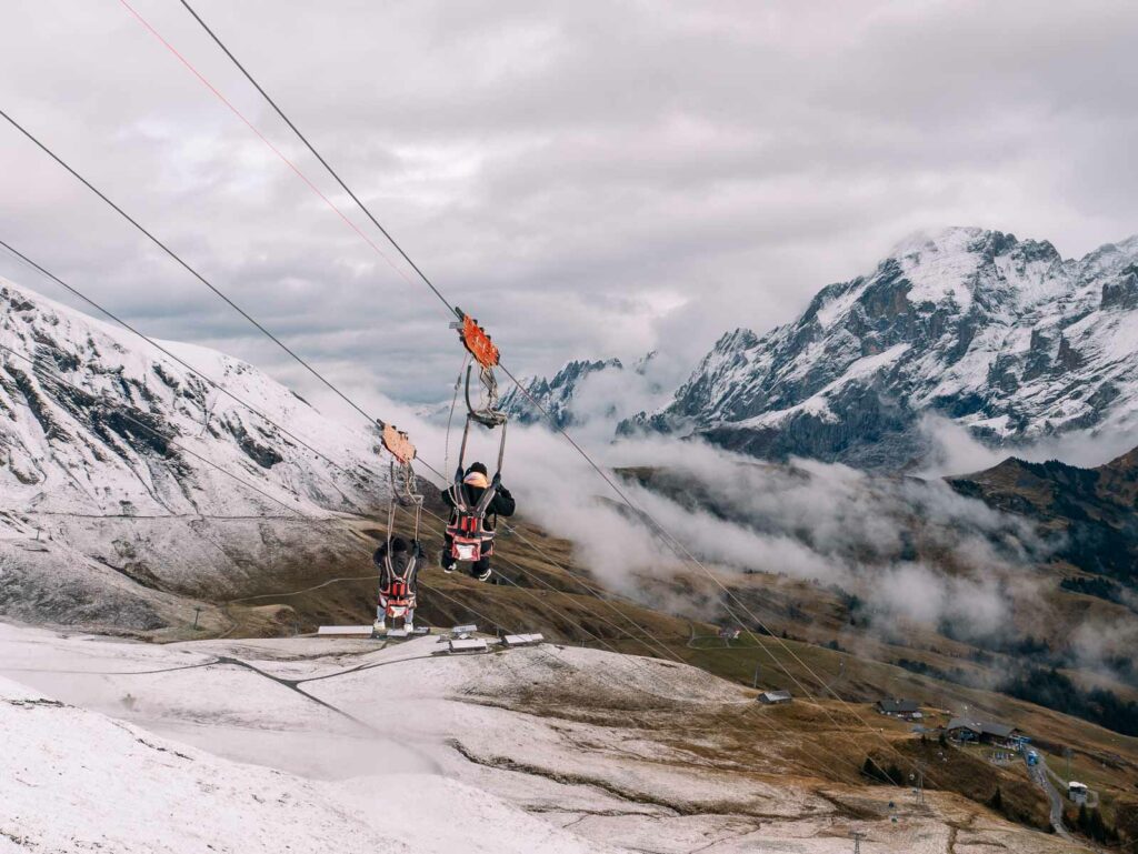 People ziplining over a snowy landscape with alpine mountains in the backdrop in Grindelwald