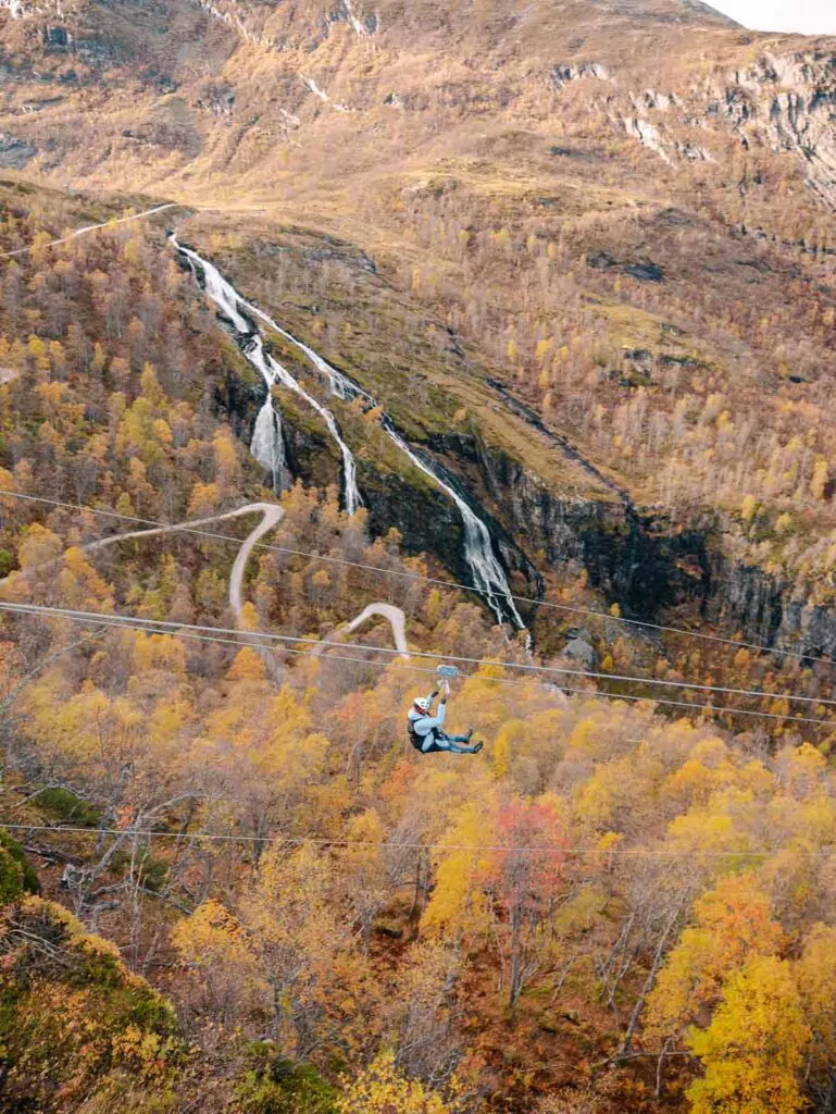 An adventurer descends on the Flam Zipline, the longest in Scandinavia, with a panoramic view of waterfalls and the colourful autumn valley below