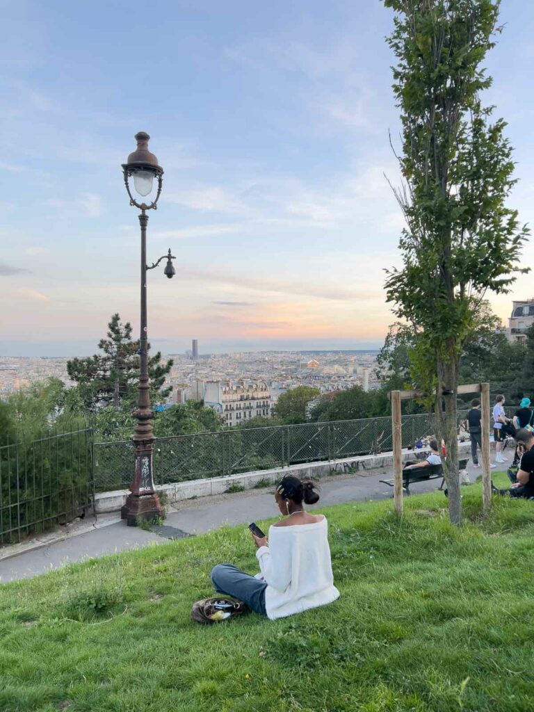 A peaceful moment captured at sunset with a person sitting on the grass at Sacré-Cœur, Paris, overlooking the cityscape with the warmth of the evening light spreading across the horizon