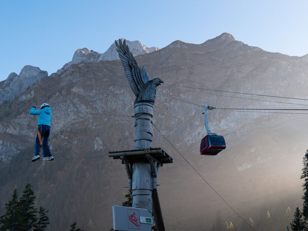 Dragon Ride cable car arriving at Mount Pilatus with Alpine peaks in the background and a young traveller on the high ropes course in front