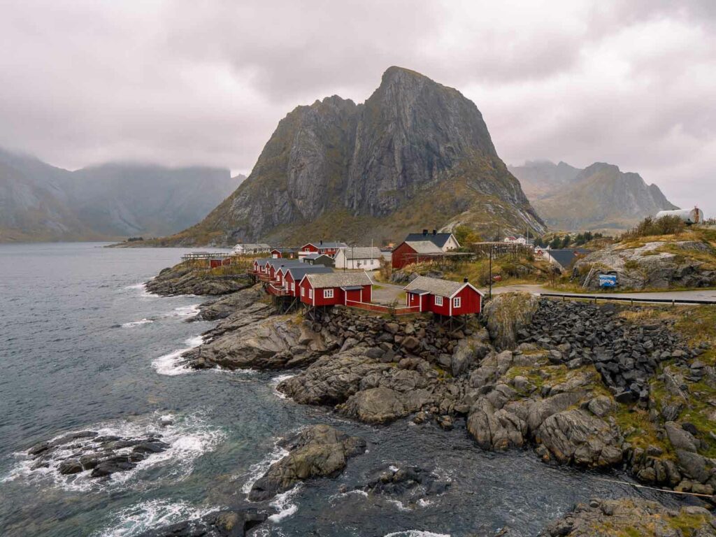 The iconic red rorbuer cabins of Hamnøy in the Lofoten Islands, with a majestic mountain backdrop and clear waters in the foreground, a quintessential stop on a Scandinavia itinerary