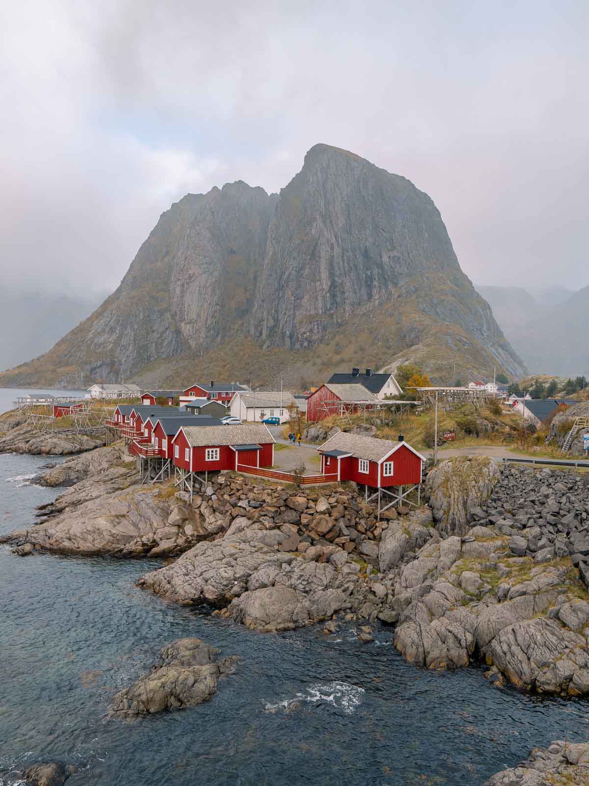 The iconic red rorbuer cabins of Hamnøy in the Lofoten Islands, with a majestic mountain backdrop and clear waters in the foreground, a quintessential stop on a Scandinavia itinerary