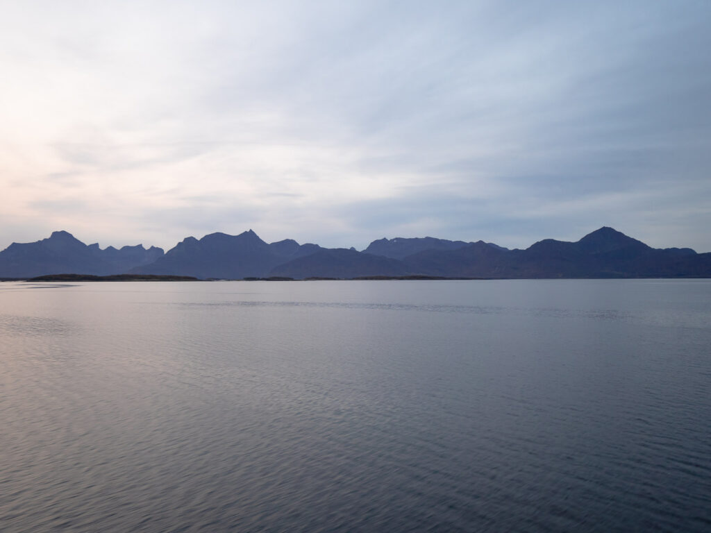 Twilight settles over the waters viewed from the express ferry between Svolvær and Bodø, where the silhouettes of distant mountains create a tranquil horizon line