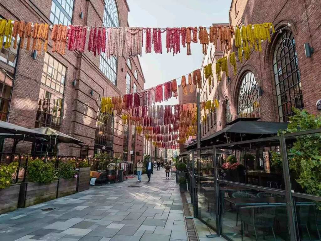 Aker Brygge district in Oslo, bustling with activity beneath a canopy of colourful hanging textiles, a modern twist on a historic waterfront area
