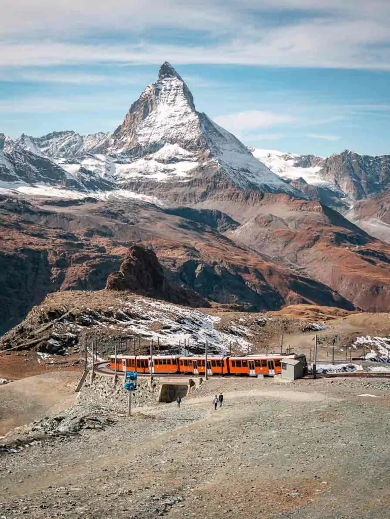 Gornergrat train passing through a rocky landscape with the iconic Matterhorn peak in the background under a clear blue sky